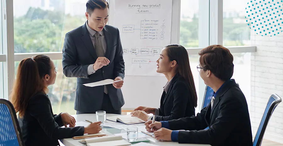 imagem de um homem em pé e três pessoas sentadas conversando num ambiente de trabalho