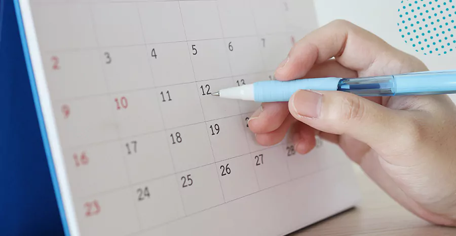 imagem de uma pessoa apontando uma caneta para um calendário de papel, representando a jornada de trabalho semanal