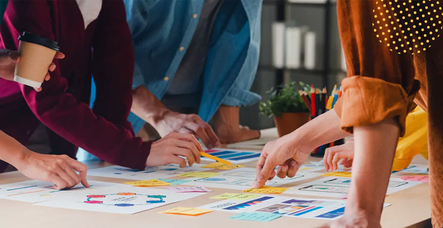 imagem de um grupo de pessoas ao redor de uma mesa apontando para folhas