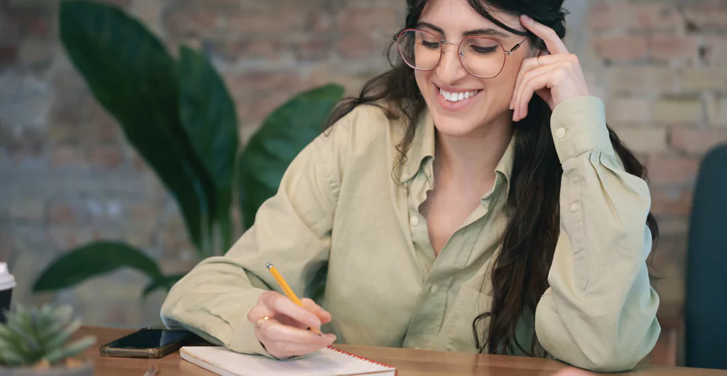 Homem de óculos e camisa verde, escrevendo em caderno sob a mesa