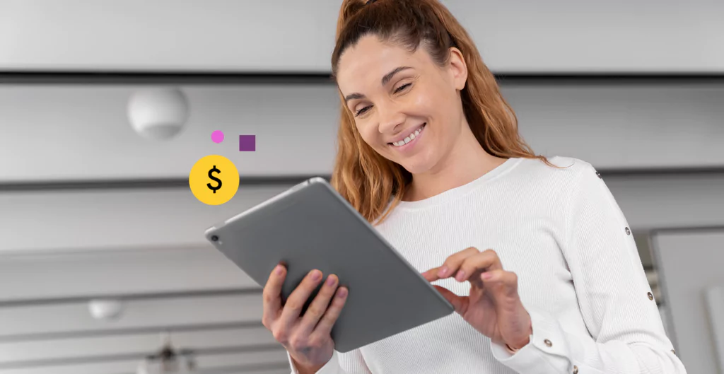 Mulher sorridente usando tablet com ícone de cifrão, representando acesso digital a benefícios financeiros.