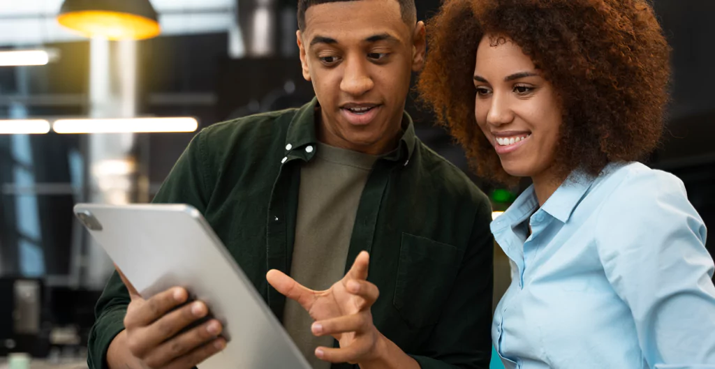 Dois jovens analisando informações em um tablet em um ambiente moderno e descontraído, demonstrando colaboração e interesse pela tecnologia.