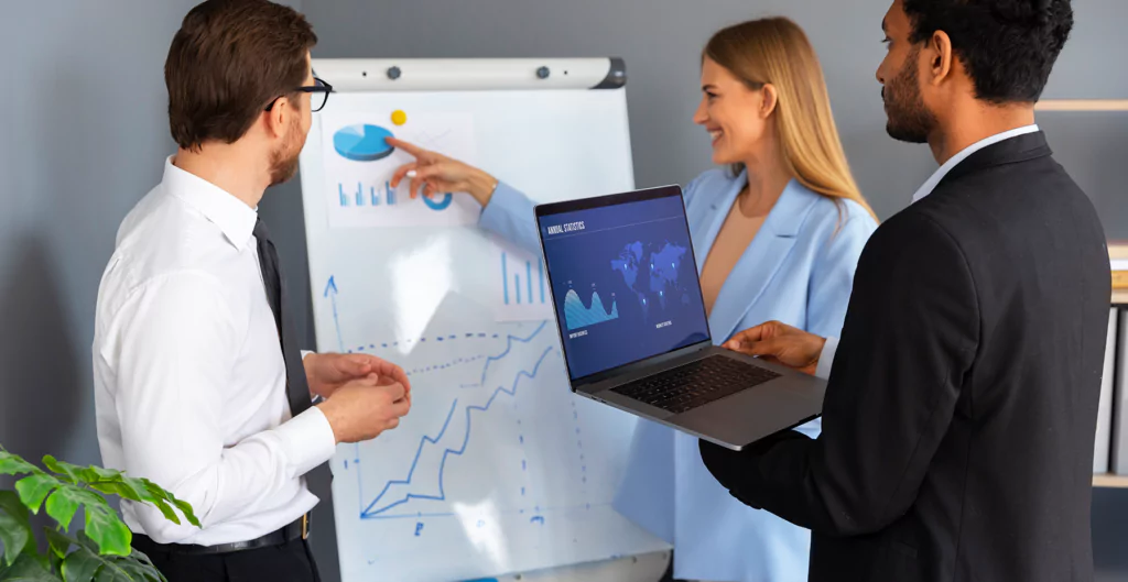 Imagem de uma apresentação de negócios, com profissionais discutindo gráficos e dados em um laptop, simbolizando trabalho em equipe e análise de mercado.