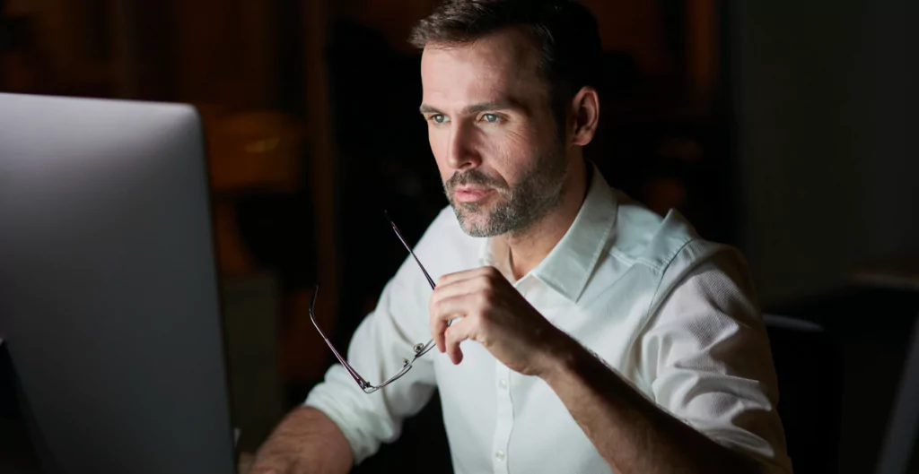 Homem atento ao computador à noite, sugerindo hora extra ou correção de ponto.