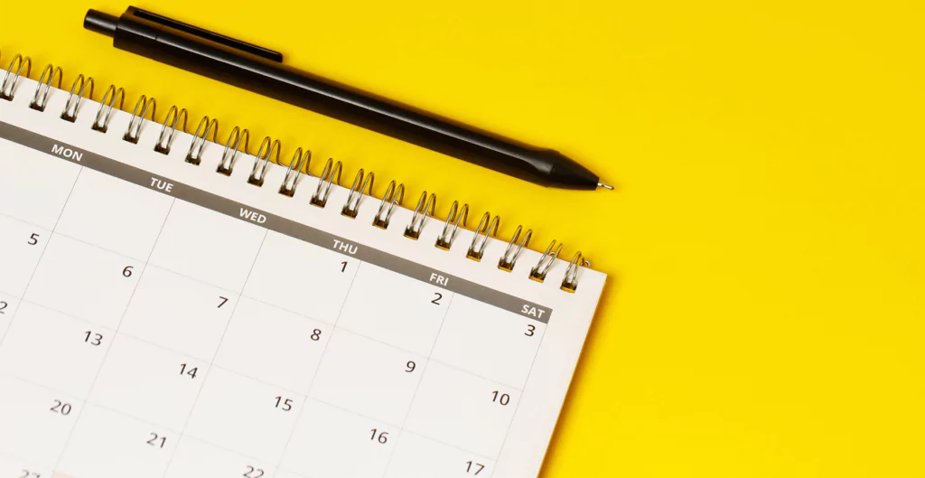 Calendário com caneta sobre fundo amarelo, indicando planejamento de feriados.