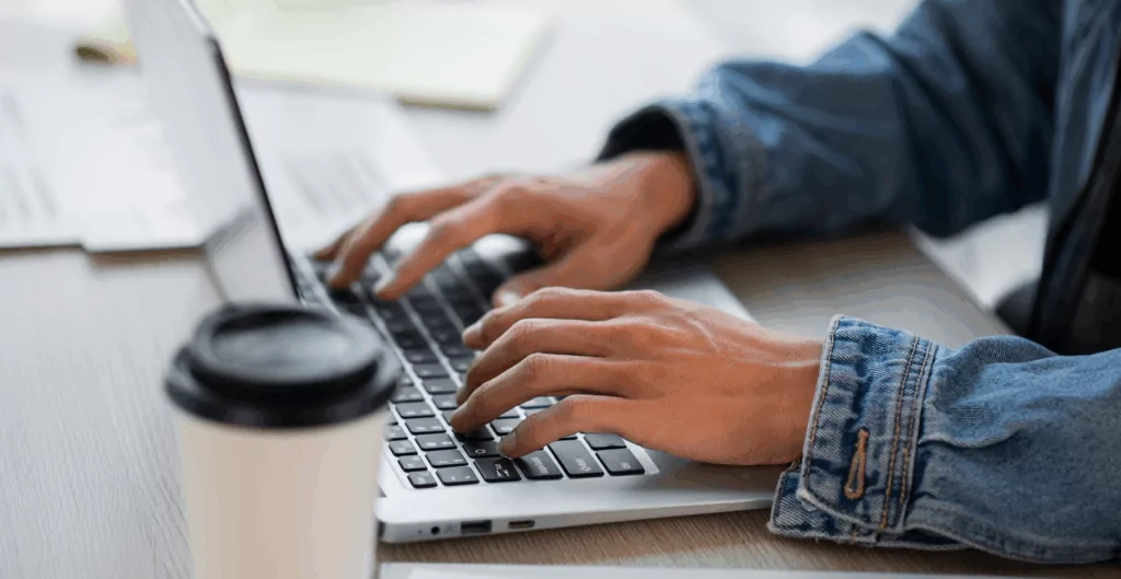 Mãos digitando em notebook com casaco jeans