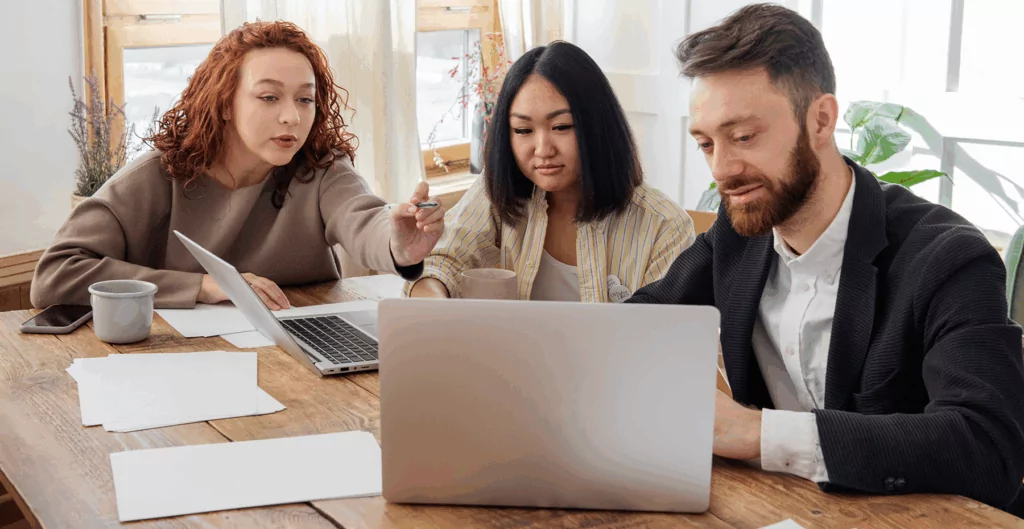 Pessoas conversando com notebooks e papeis sobre a mesa e escritório ao fundo 