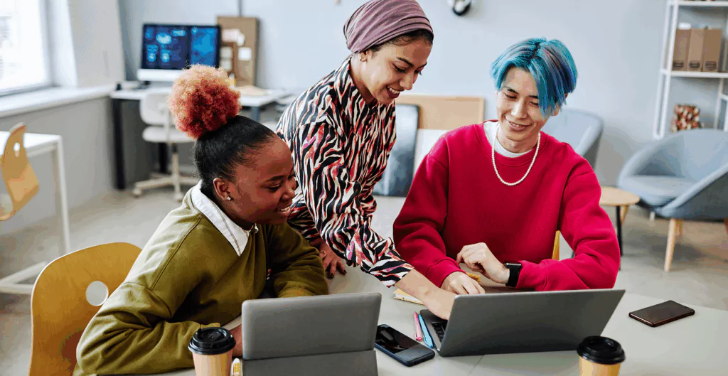 Grupo de jovens profissionais trabalhando juntos em um ambiente de escritório moderno, com laptops e computadores, promovendo colaboração e inovação.