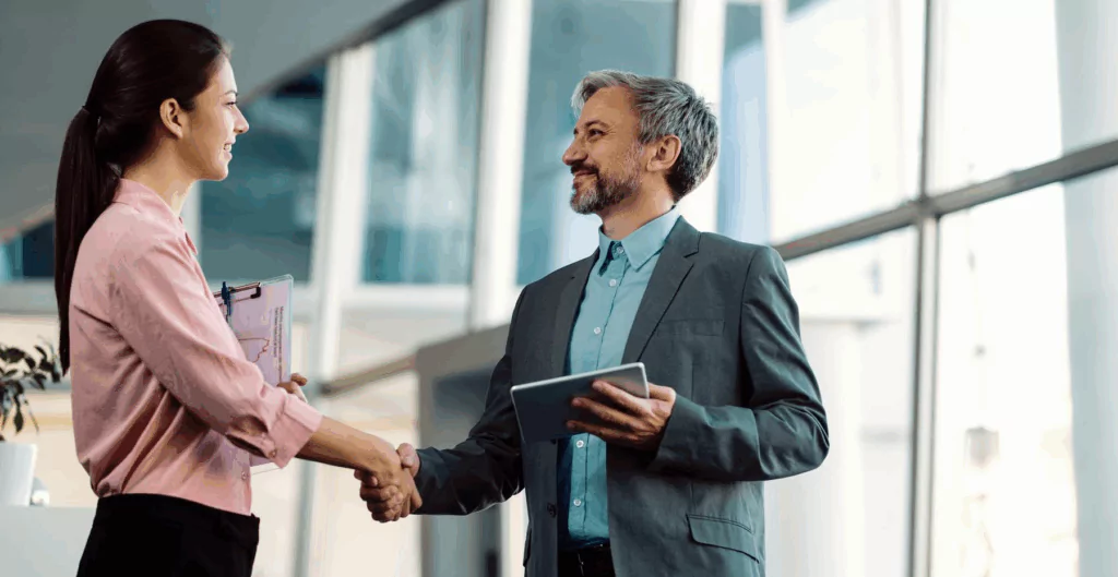Homem e mulher de negócios se cumprimentando com aperto de mão em ambiente corporativo moderno, simbolizando parceria ou fechamento de negócios.