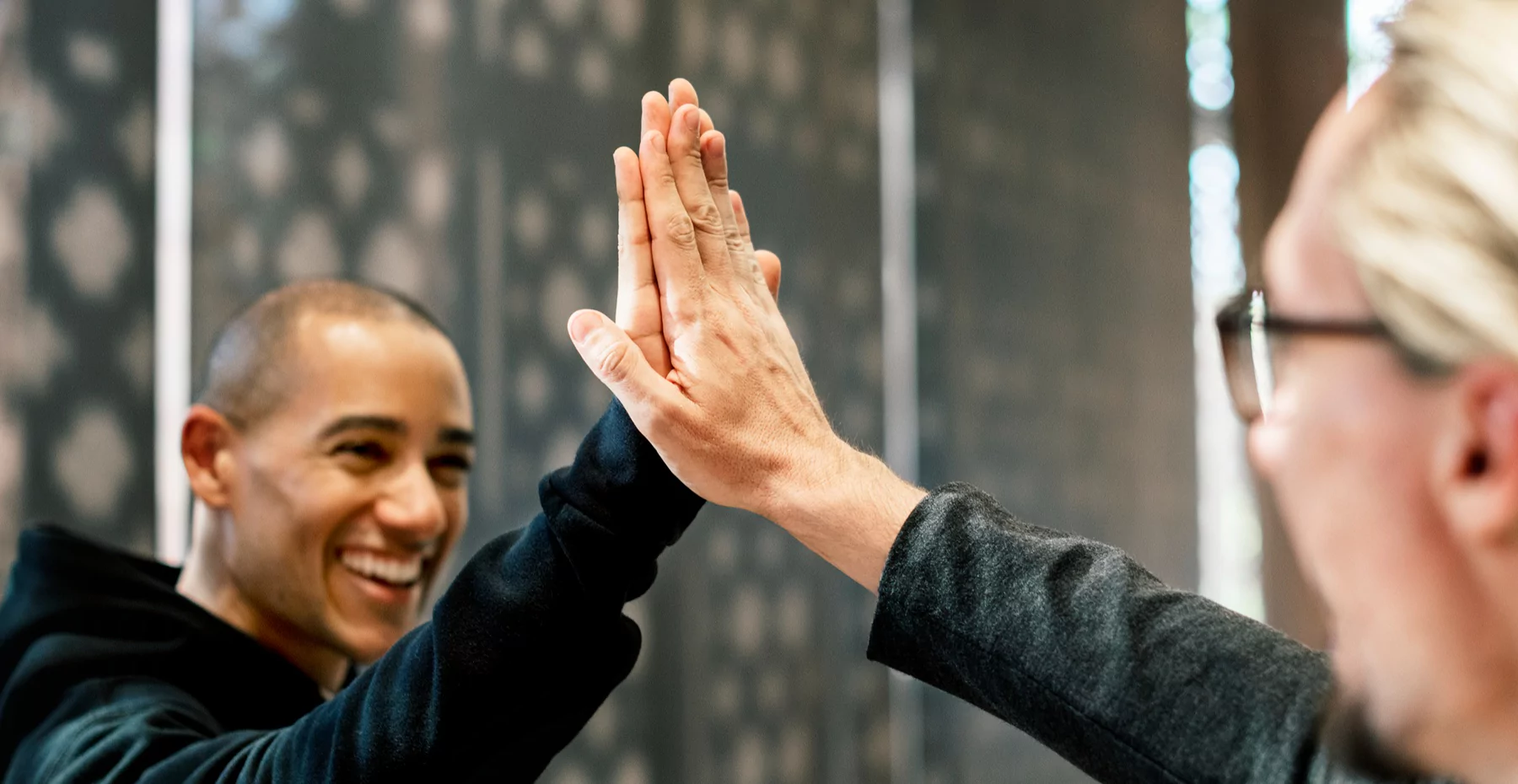 Jovem e idosa trocam um high five, simbolizando amizade e conexão, em ambiente urbano com luz natural, destacando entusiasmo e união.